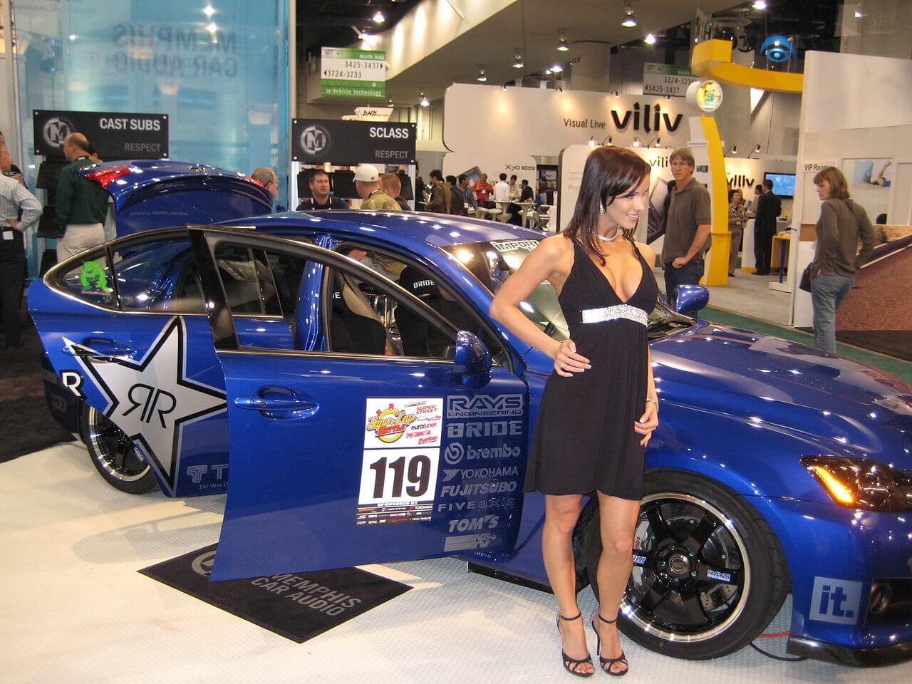 A woman standing next to a blue car on display
