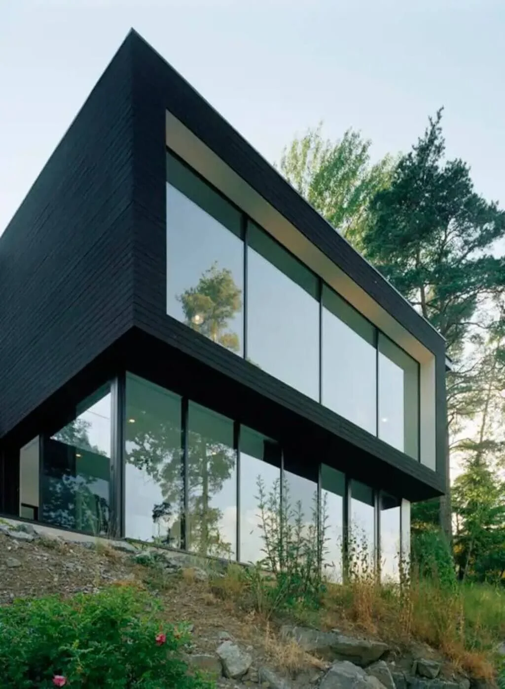 A black house with lots of windows sitting on top of a hill
