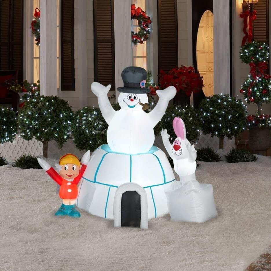 A large inflatable snowman and a small boy standing in front of a house
