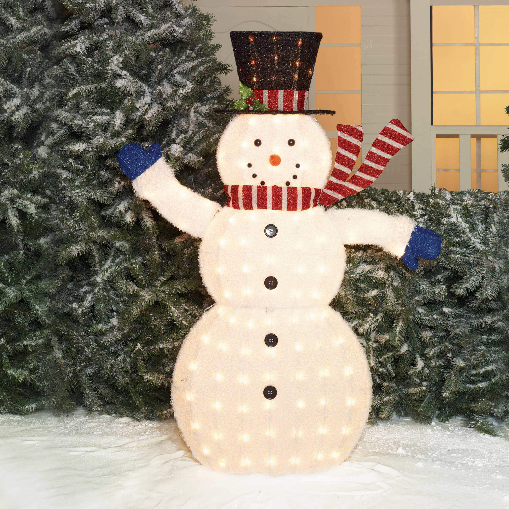 A lighted snowman standing in front of a christmas tree
