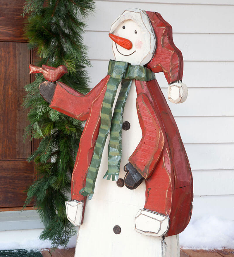 A wooden snowman standing next to a christmas wreath
