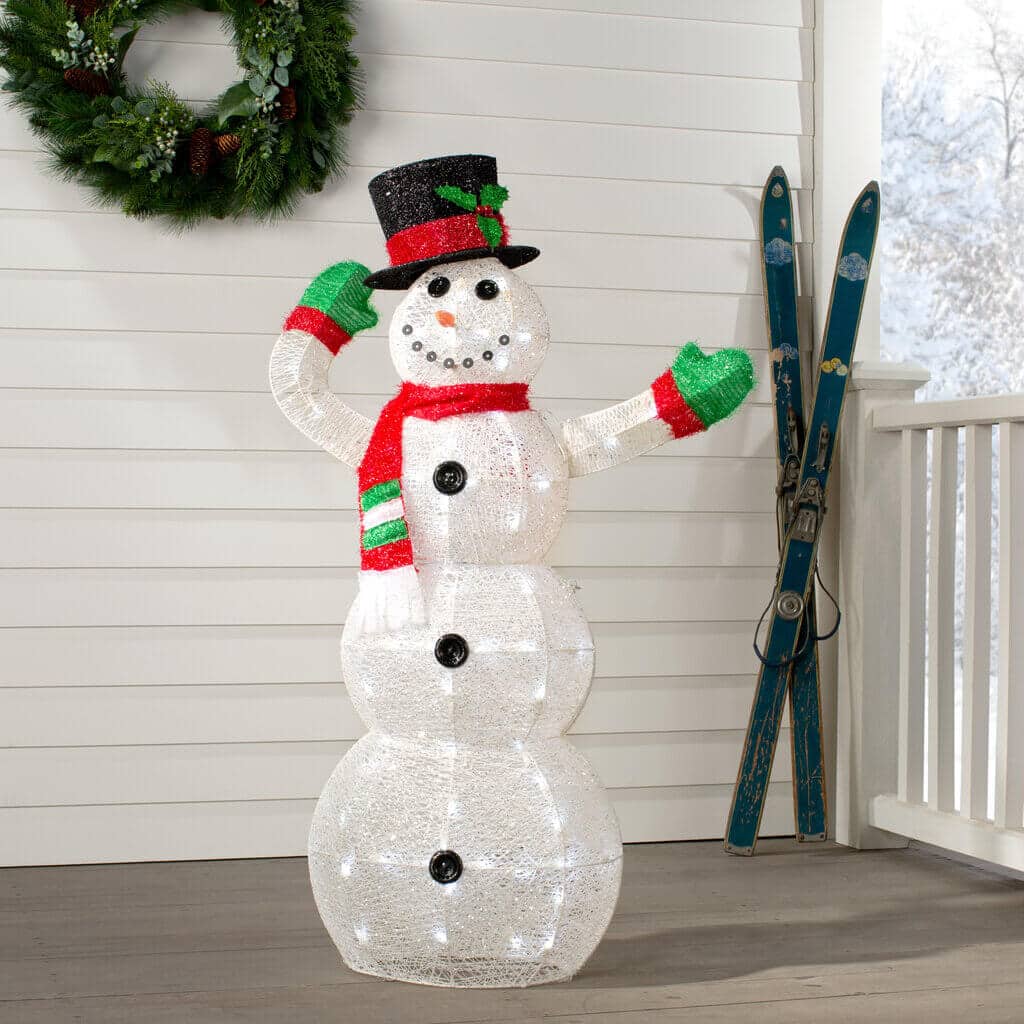 A lighted snowman standing on a porch next to a wreath
