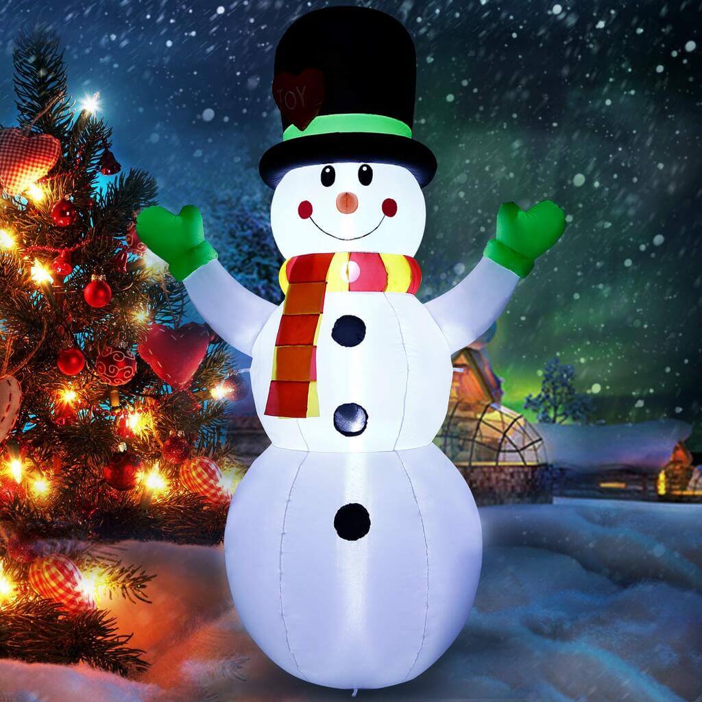 A lighted snowman standing next to a christmas tree
