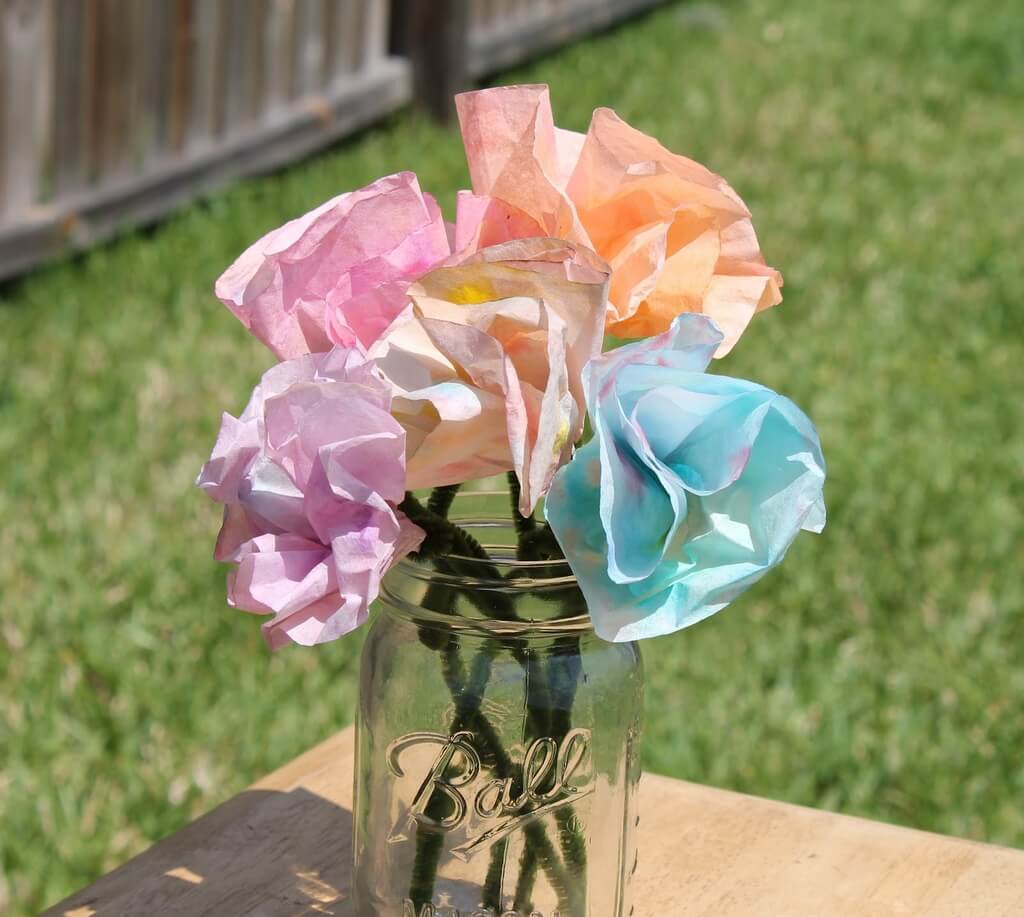 A mason jar filled with paper flowers on top of a wooden table
