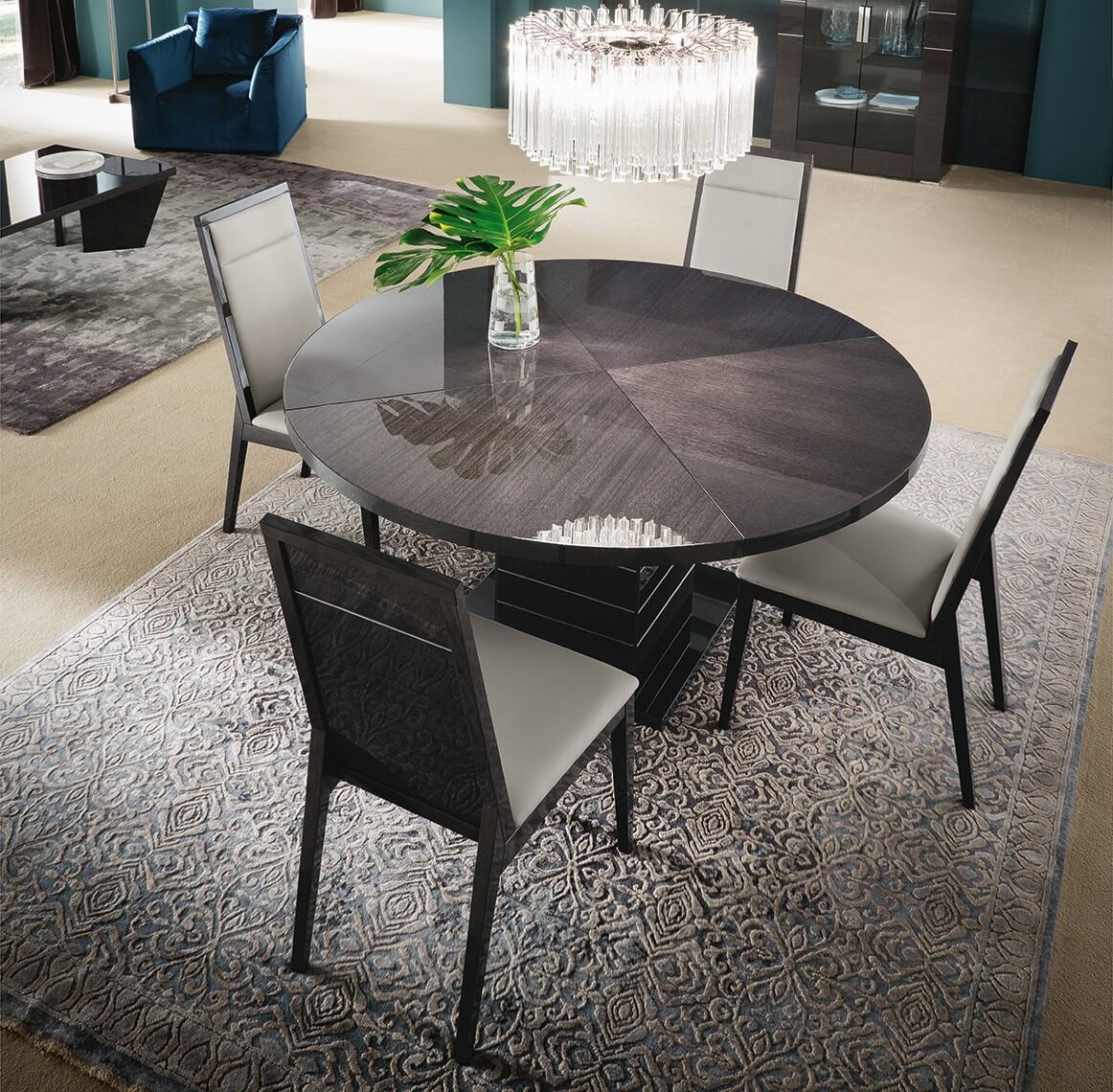 A  round dining room table with a vase of flowers on top of it with chandelier
