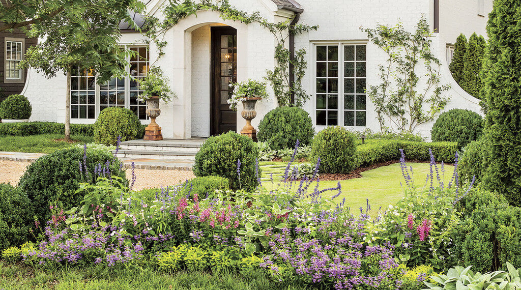 A white house with lots of flowers and bushes around it
