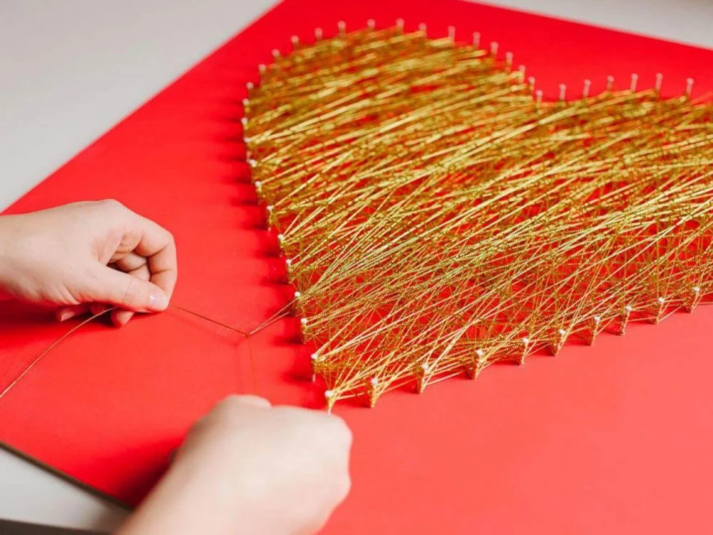 A person making a heart out of gold thread
