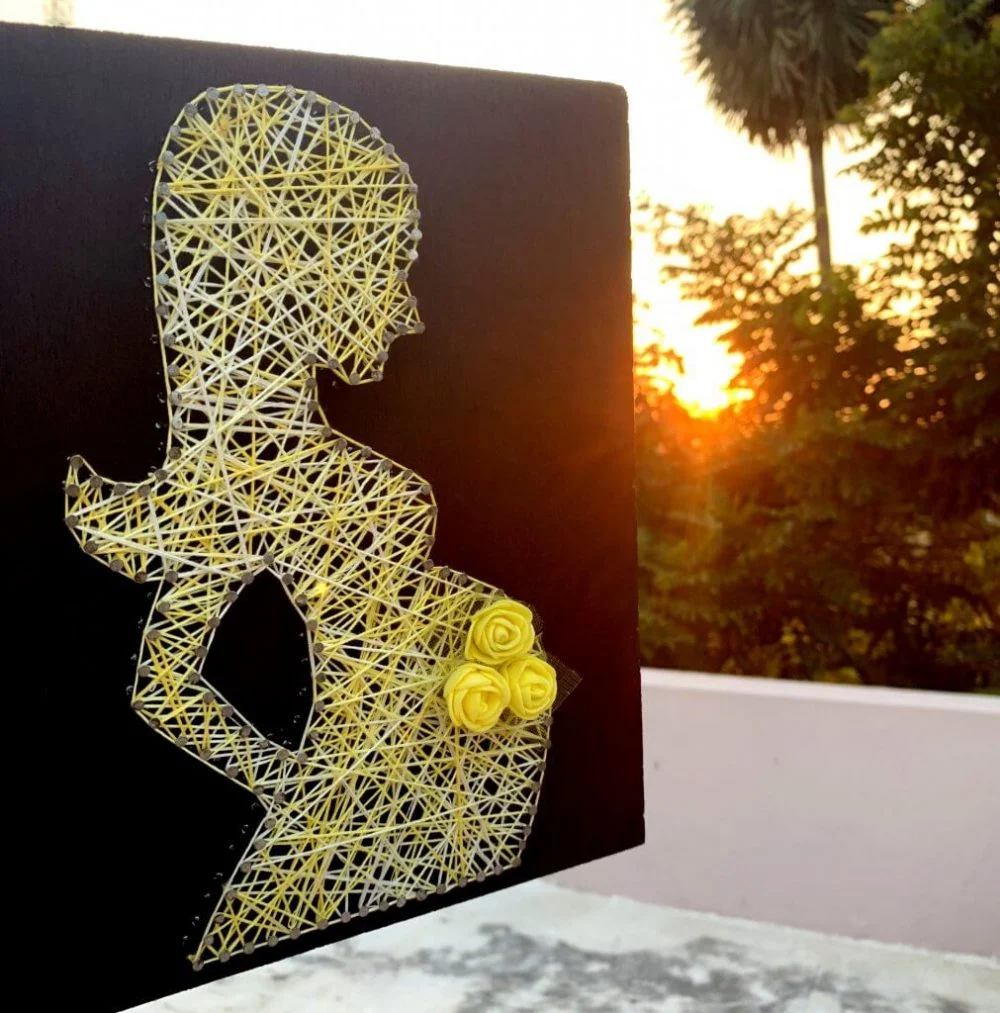 A string art picture of a woman with yellow roses

