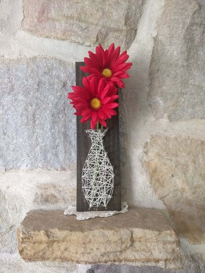 A vase with a red flower on top of a stone wall
