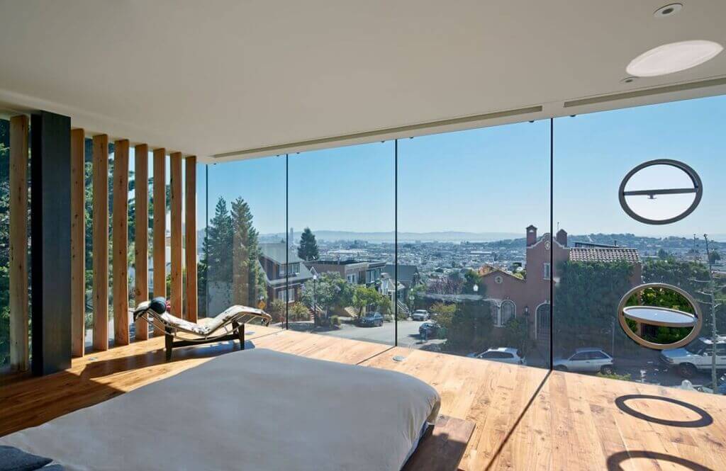 A bedroom with glass walls overlooking a city.