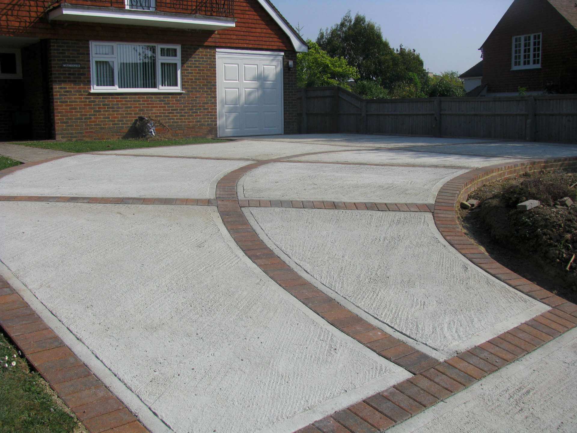 A driveway with a brick walkway and a garage in the background
