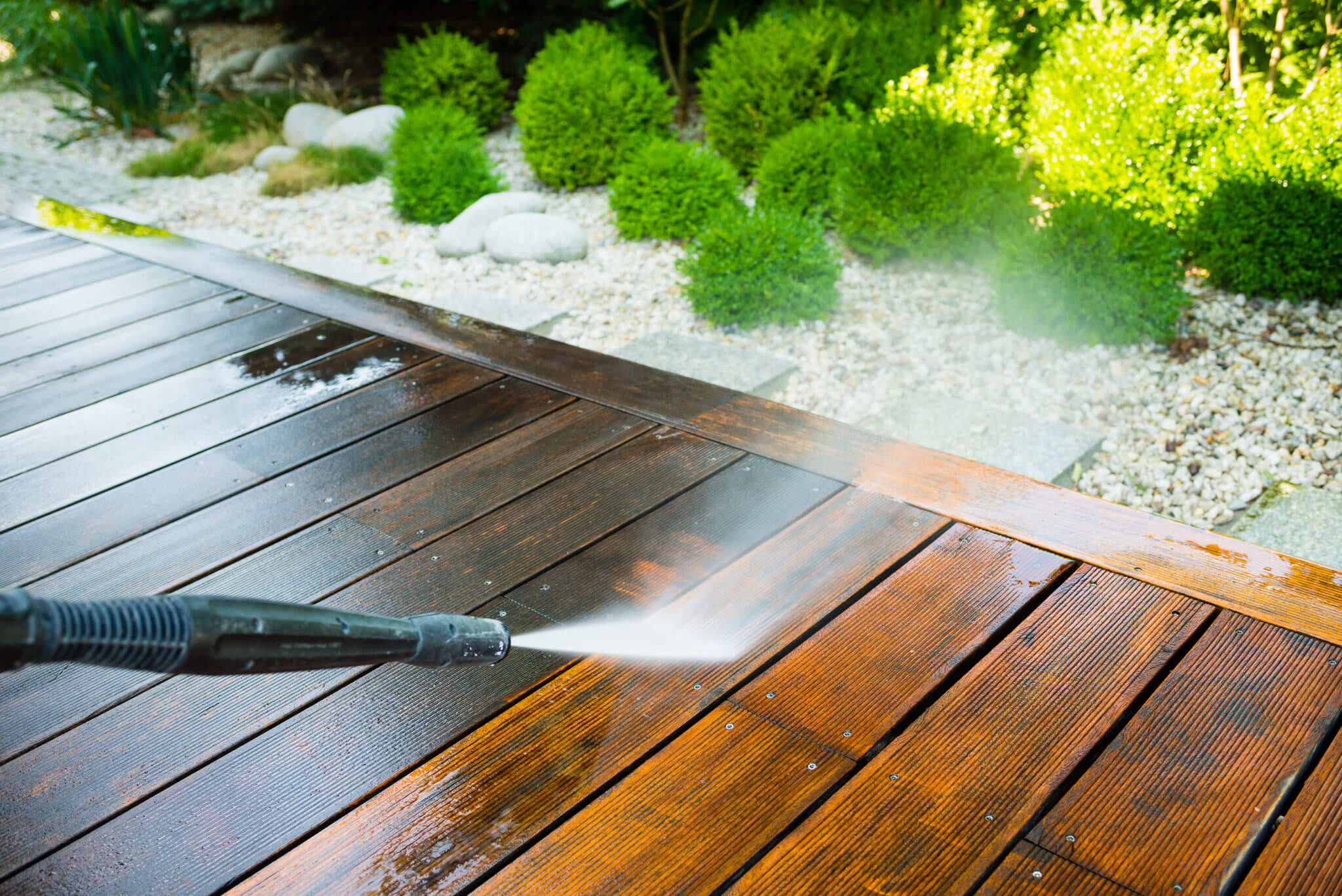 A person using a pressure washer on a wooden deck
