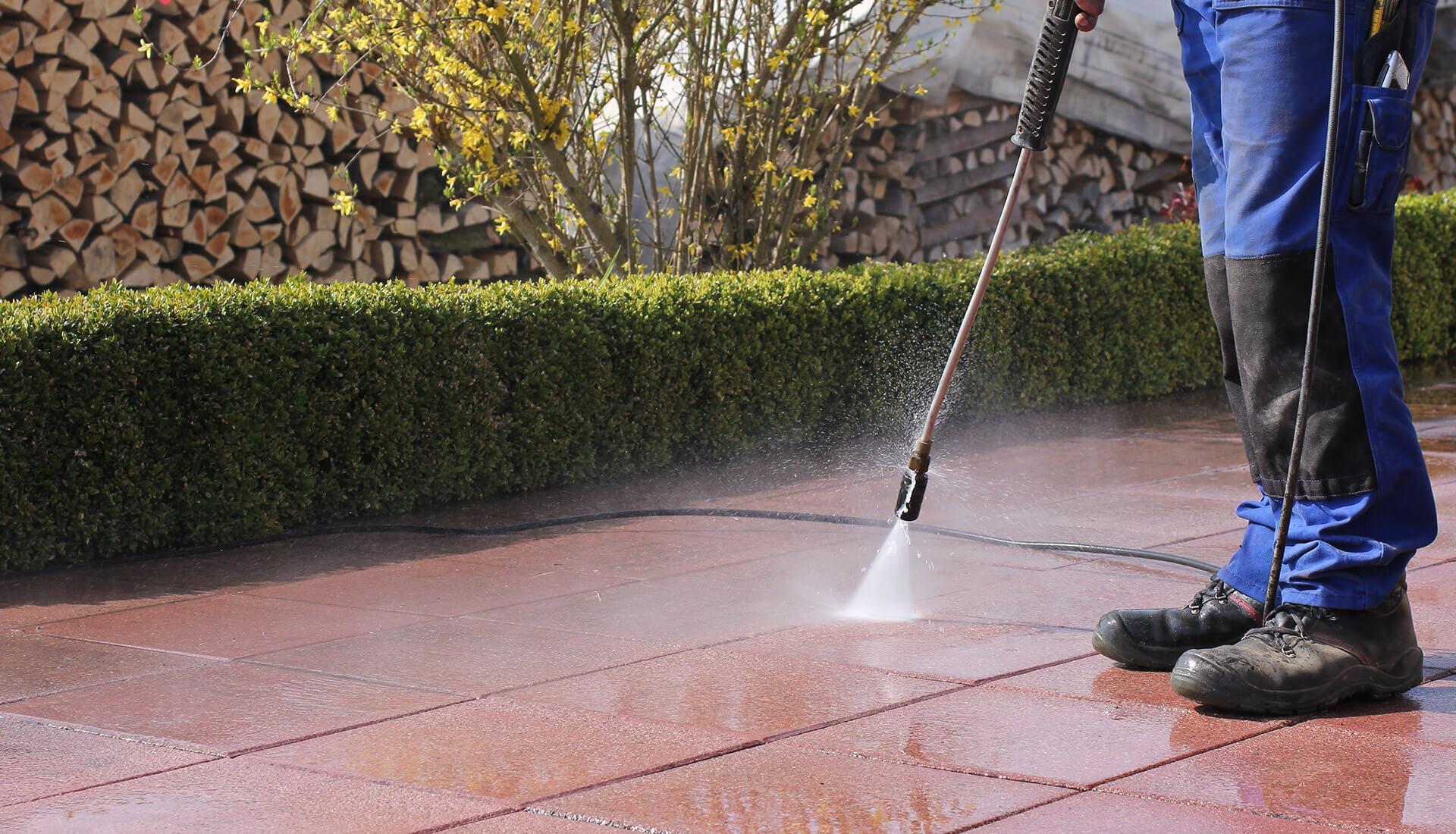 A person using a pressure washer to clean a sidewalk
