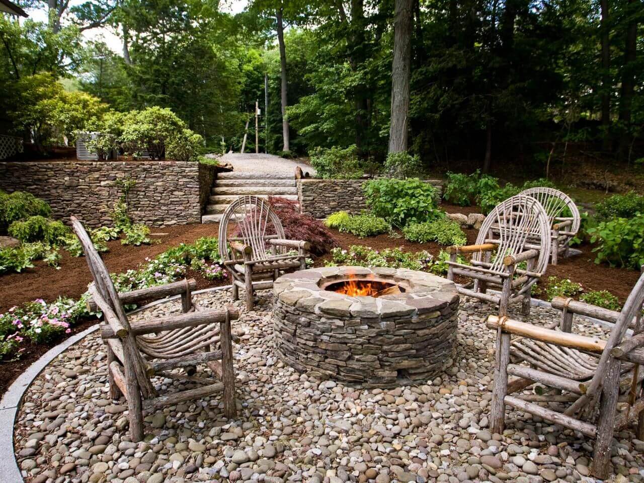 A stone fire pit surrounded by chairs and trees
