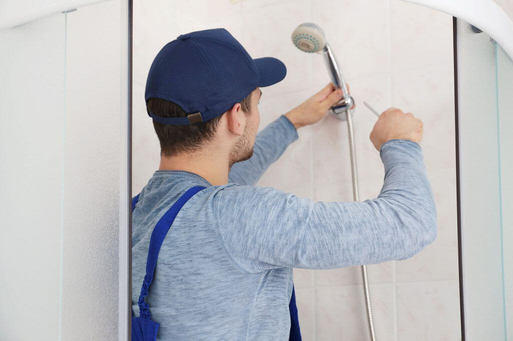 A man in a blue hat is fixing a shower head
