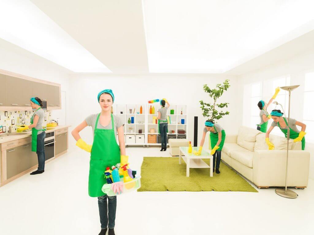 A woman in a green apron holding a bucket of cleaning supplies
