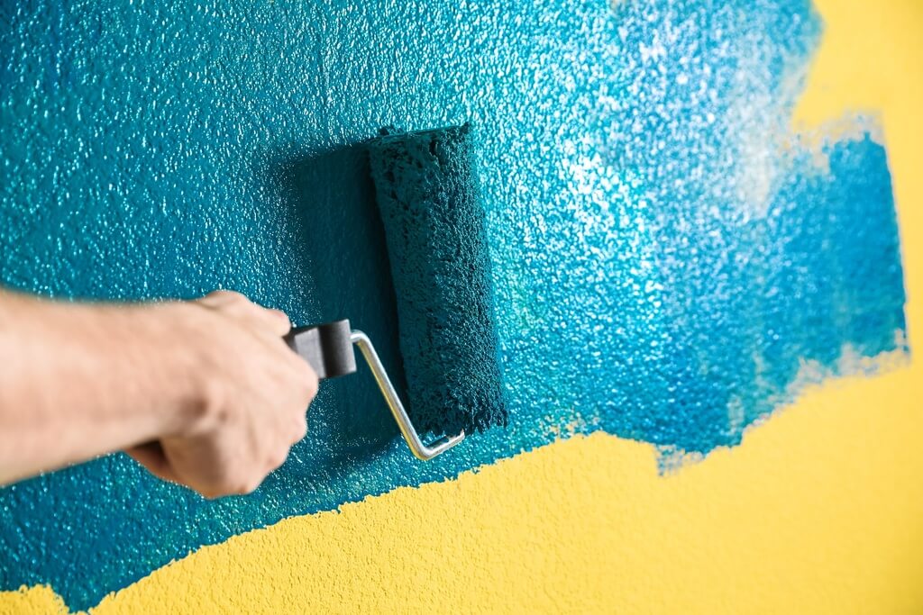 A person using a paint roller to paint a wall
