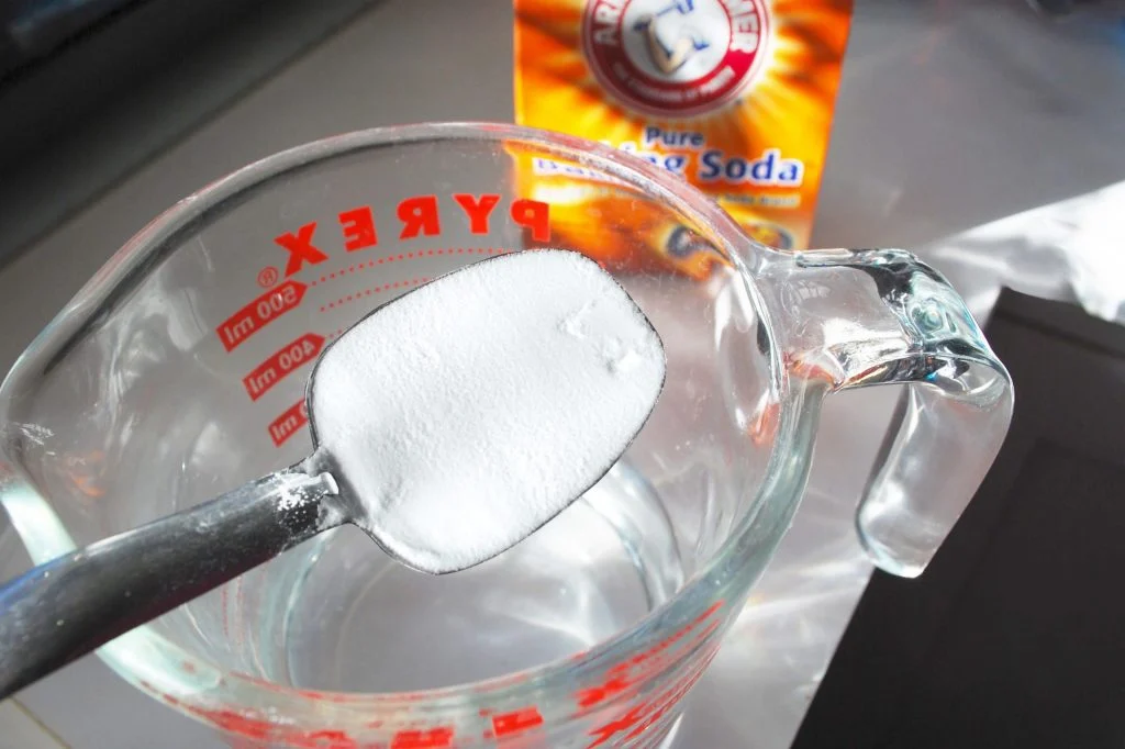 A measuring cup filled with Baking Soda and a spoon
