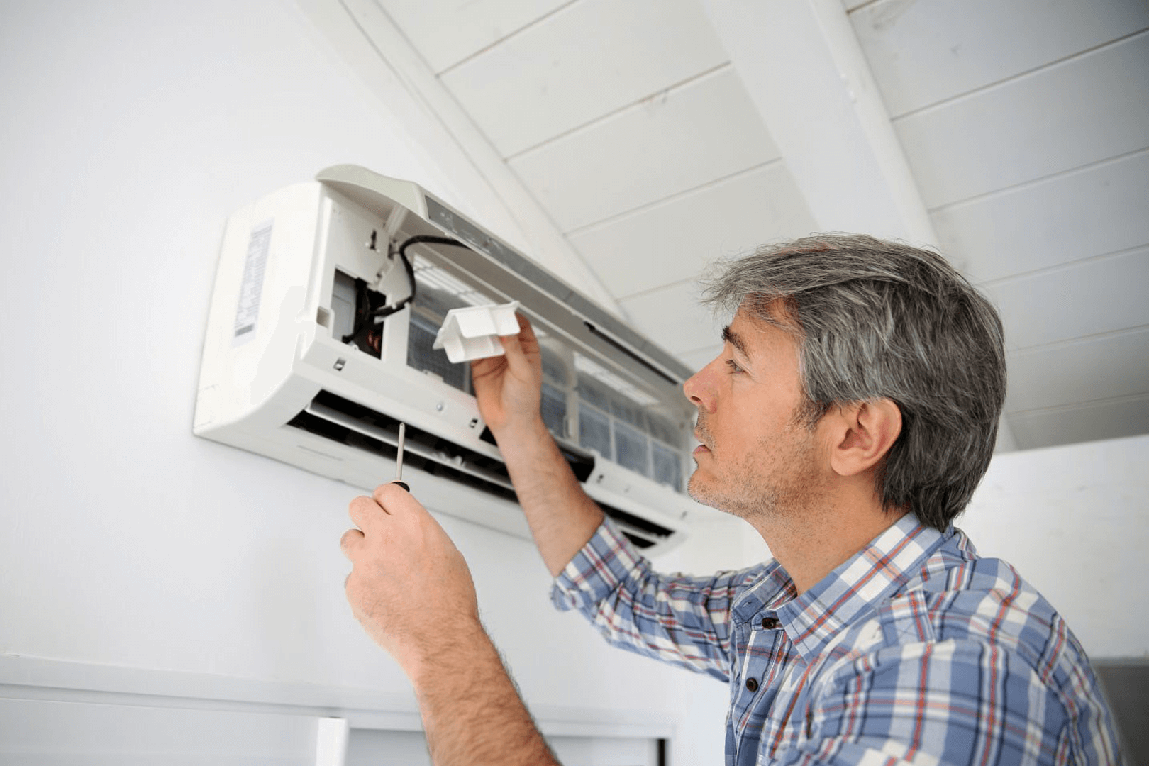 A man adjusting an air conditioner on a wall
