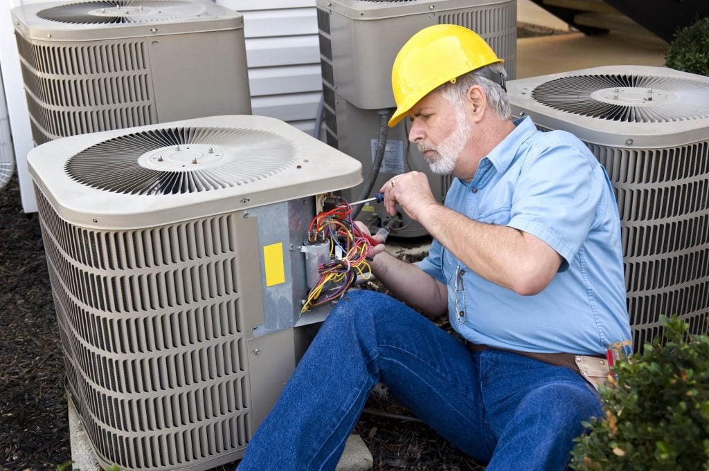 A man sitting on the ground next to air conditioners
