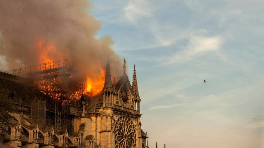 A large cathedral on fire with smoke billowing out of it
