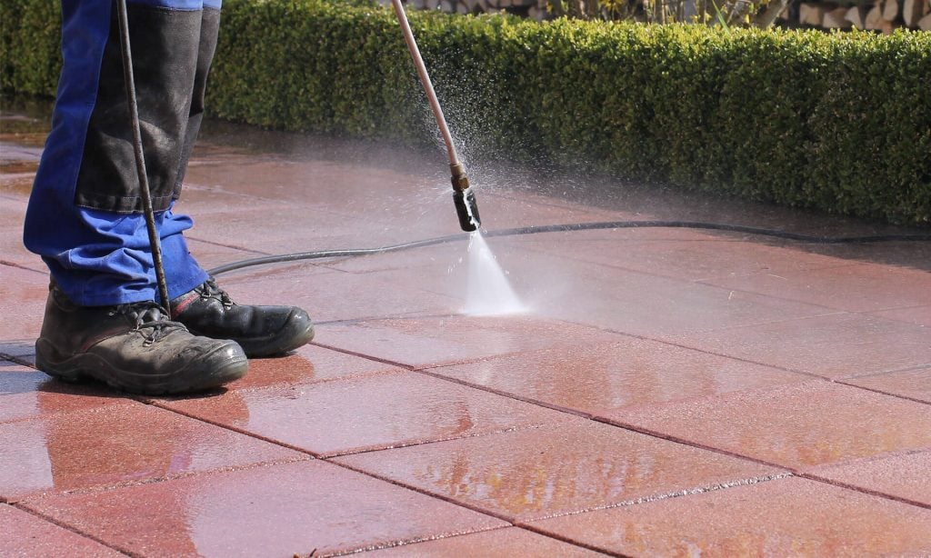 A person using a pressure washer to clean a sidewalk
