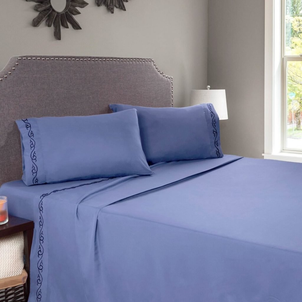 A bed with blue sheets and pillows in a bedroom
