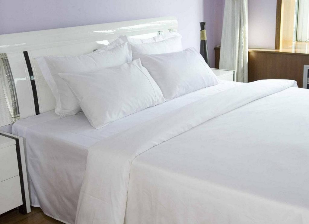 A bed with white sheets and pillows in a room
