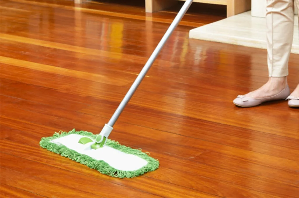 A woman cleaning a wooden floor with a mop
