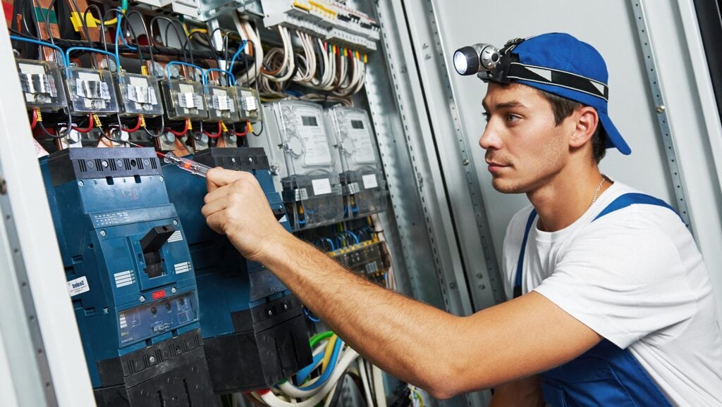 A man in a blue hat working on a switch box

