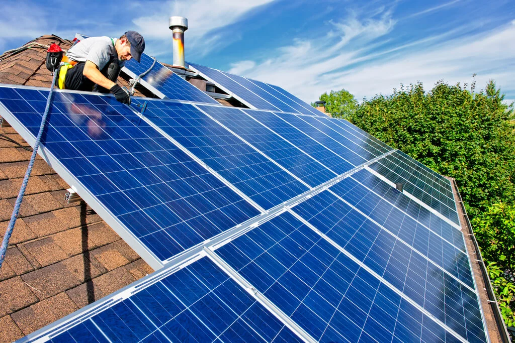 A man on a roof installing a solar panel
