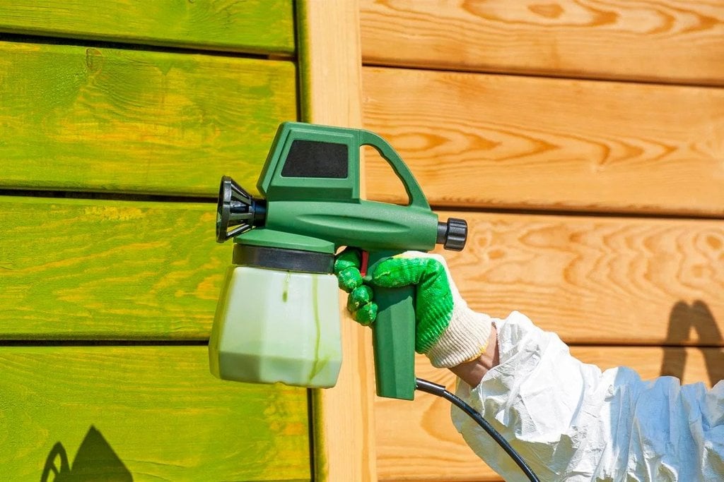 A person spraying a green sprayer on a wooden wall
