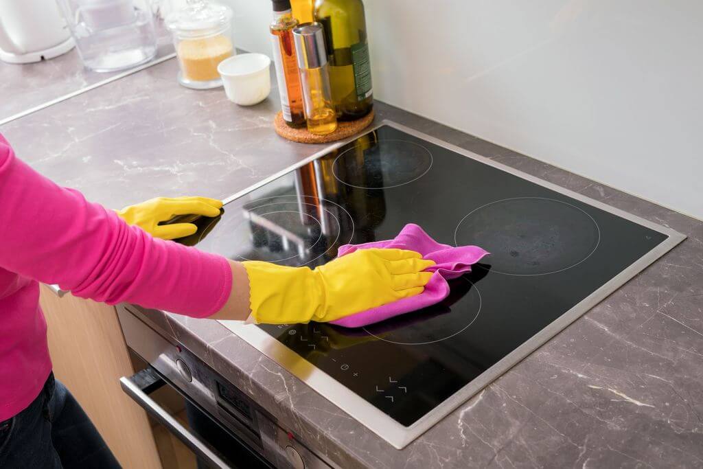 A woman in yellow gloves is cleaning a stove
