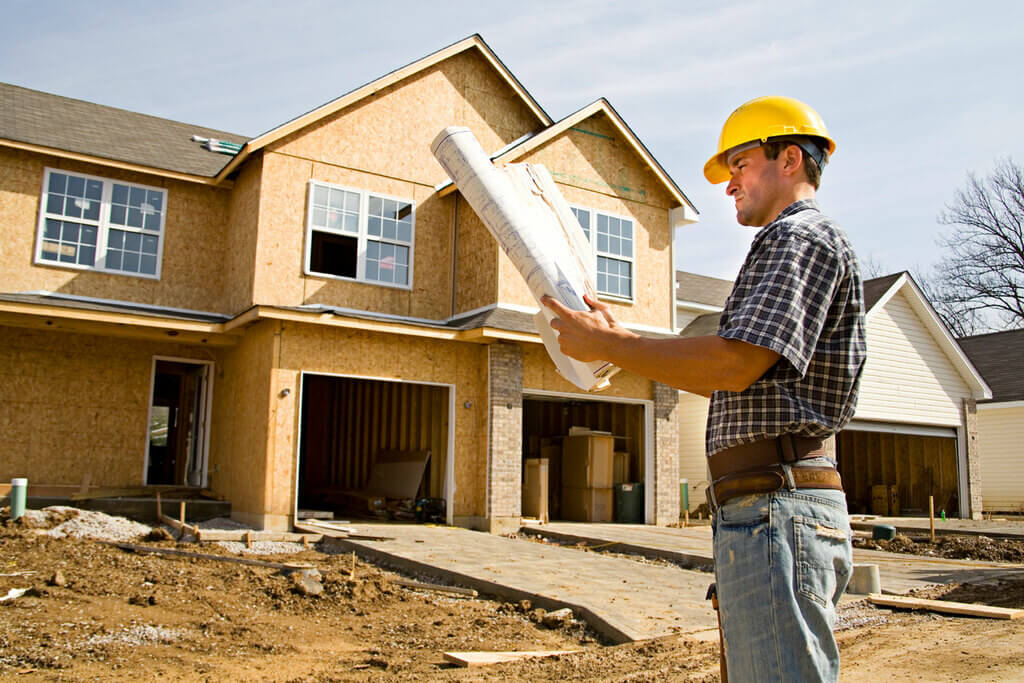 A man in a hard hat holding a blueprint in front of a house
