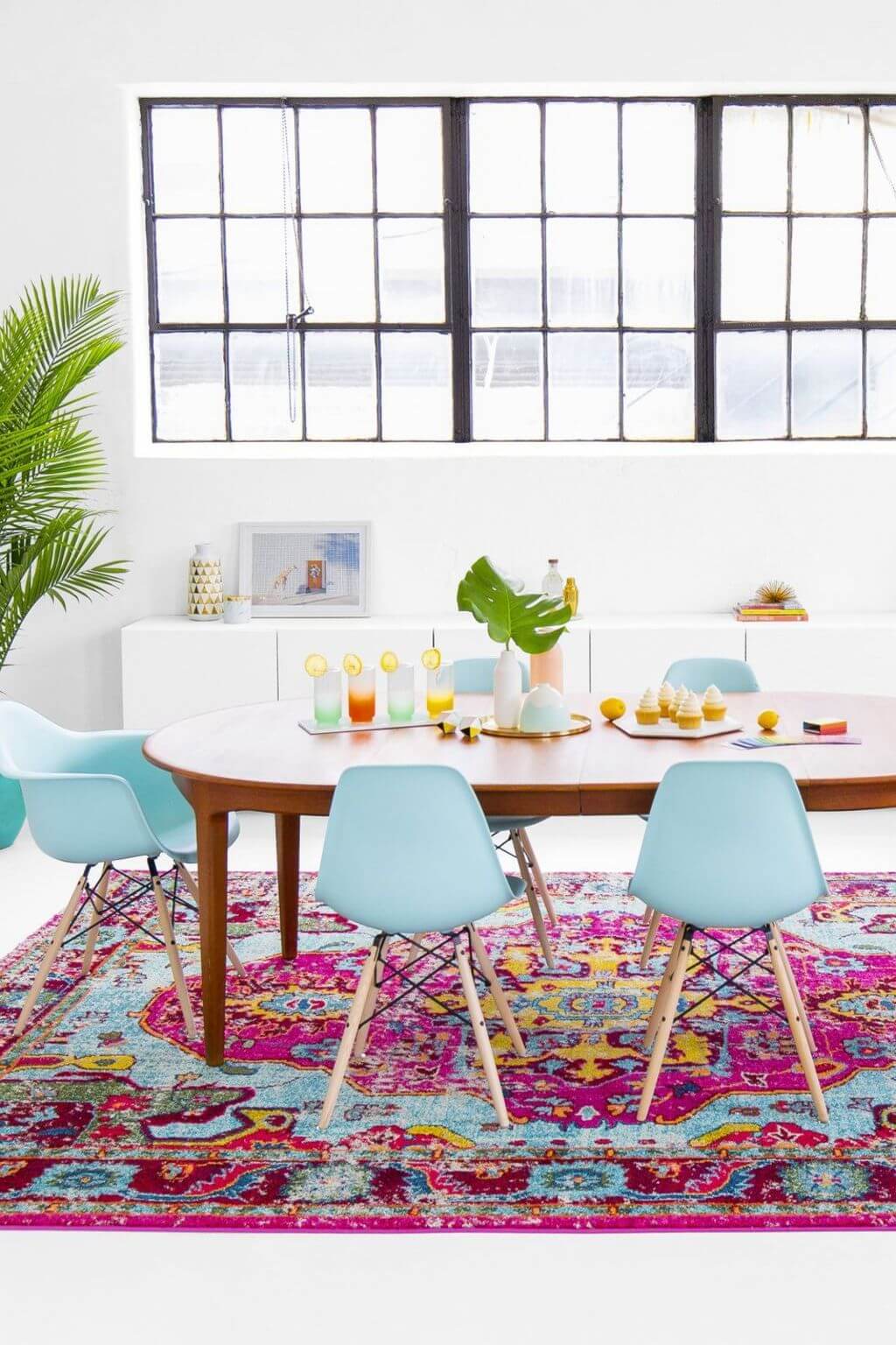A dining table with blue chairs and a colorful rug
