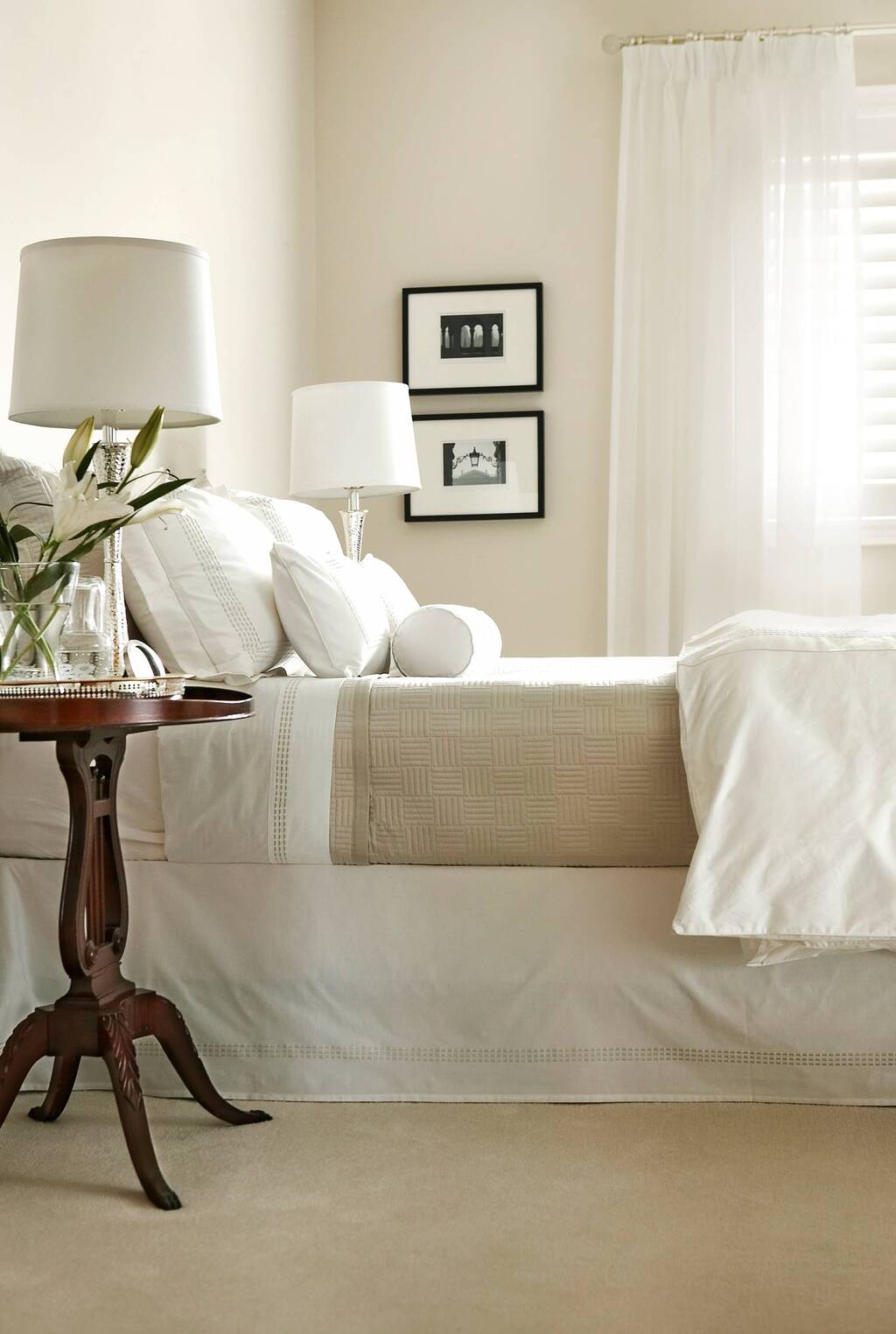 A bedroom with a bed and a table with a vase of flowers on it
