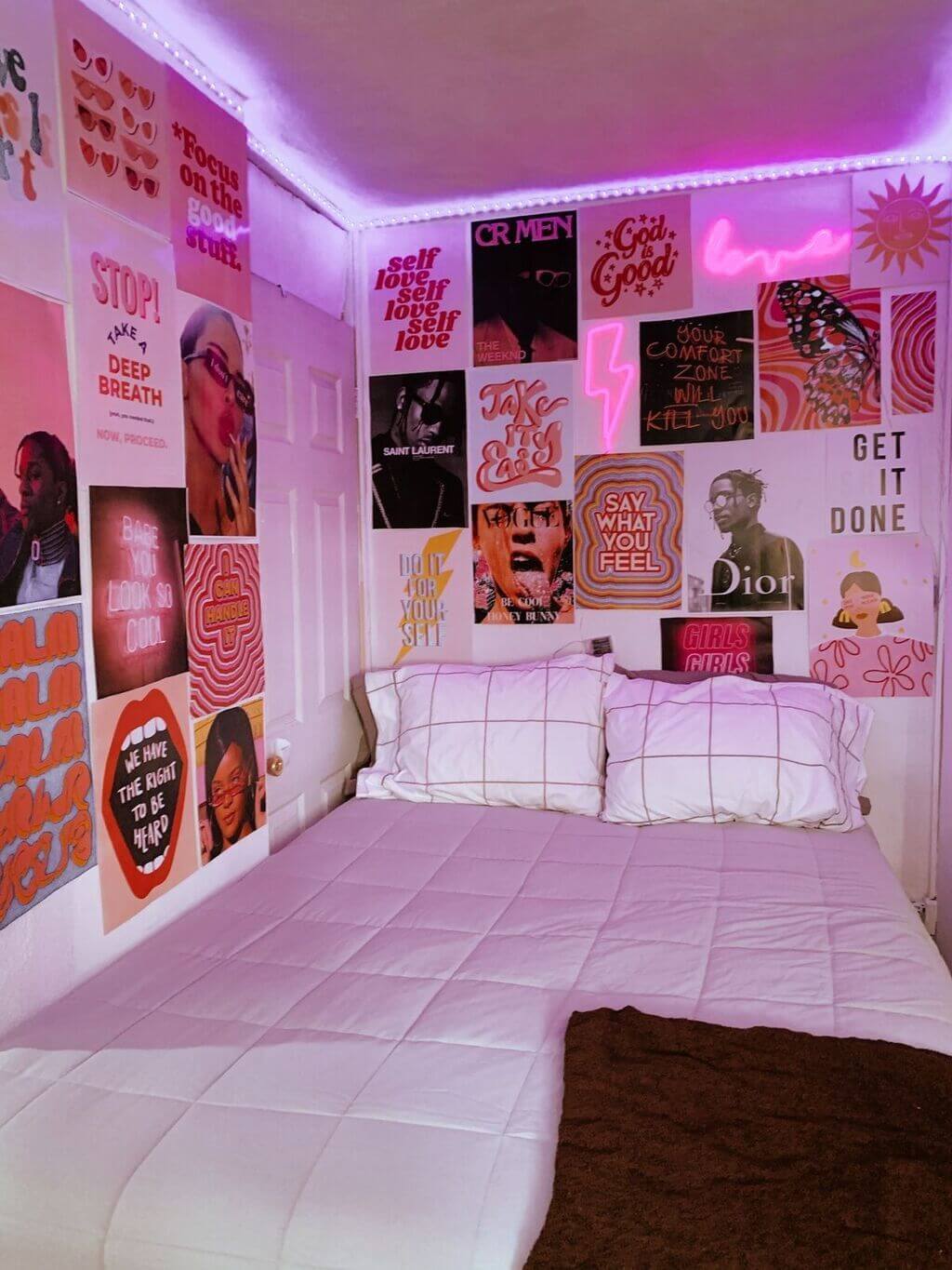 A bed with a pink comforter in a room with posters on the wall
