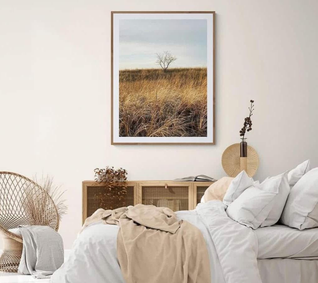A bedroom with a bed, wicker chair and a picture hanging on the wall
