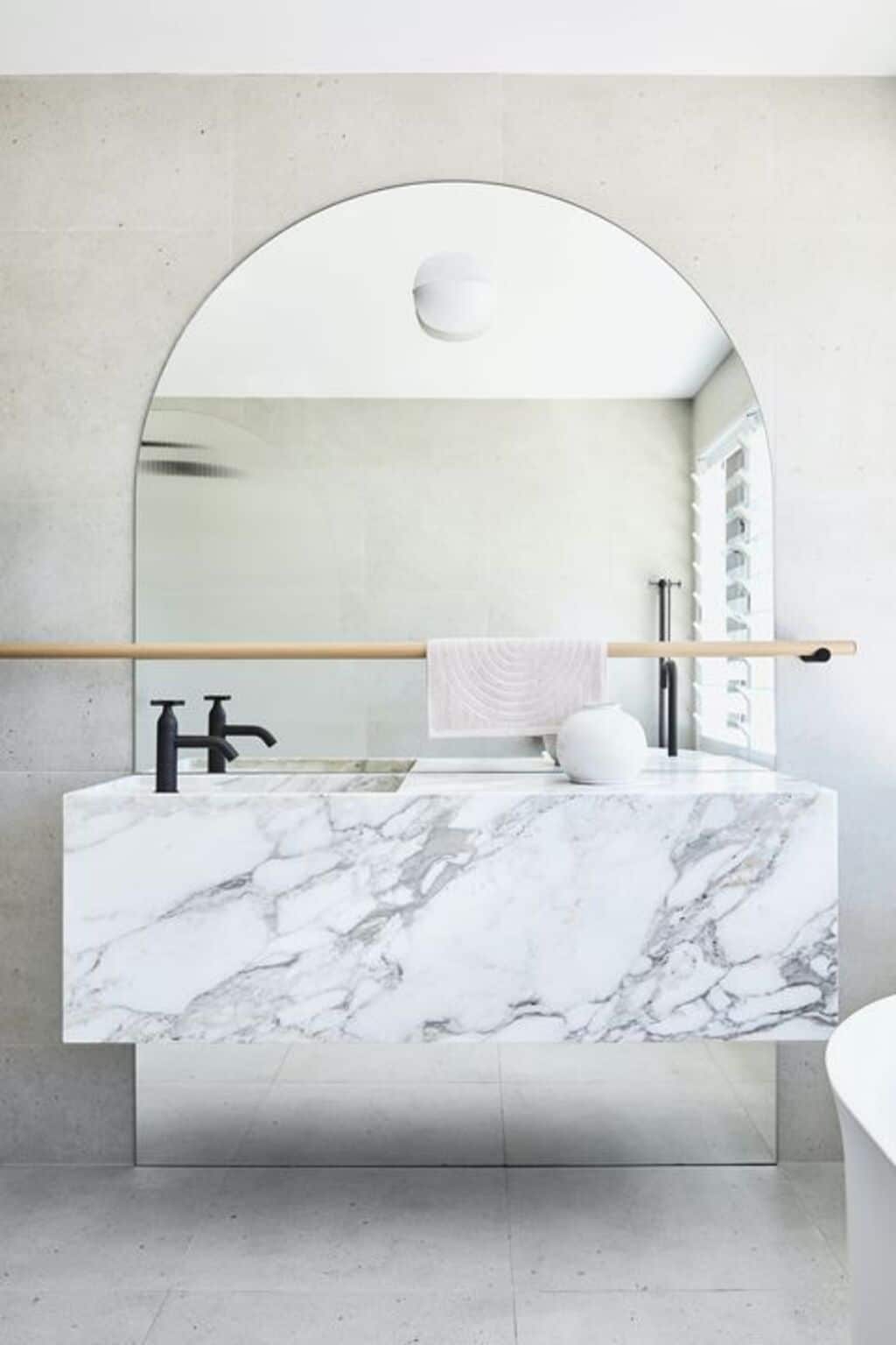 A bathroom with a marble counter top and a round mirror
