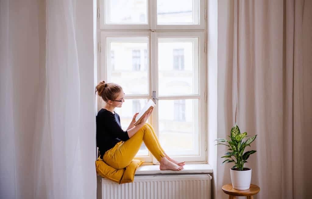 A woman sitting on a window sill looking out the window