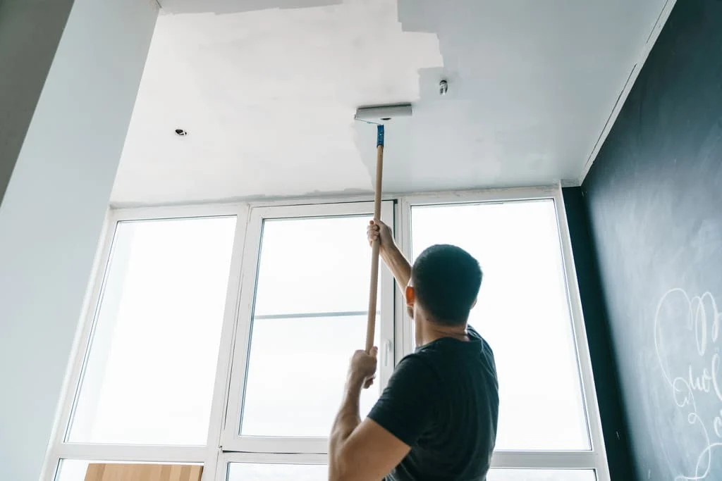 A man is painting the ceiling of a room
