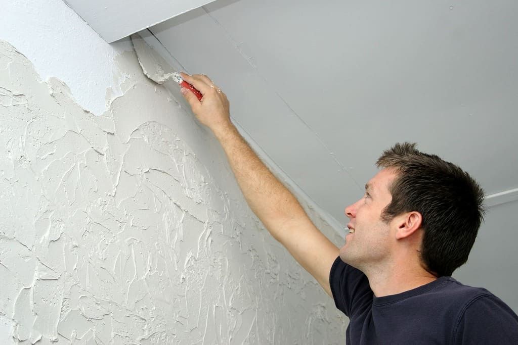 A man is painting a wall with white paint
