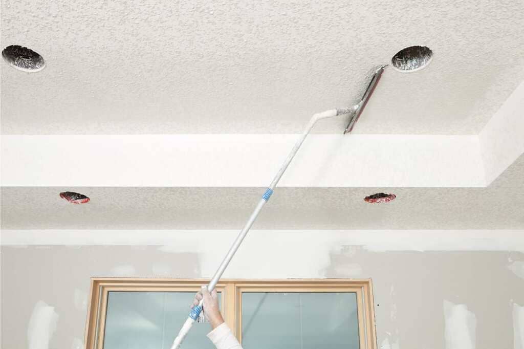 A person is painting a ceiling with a paint roller
