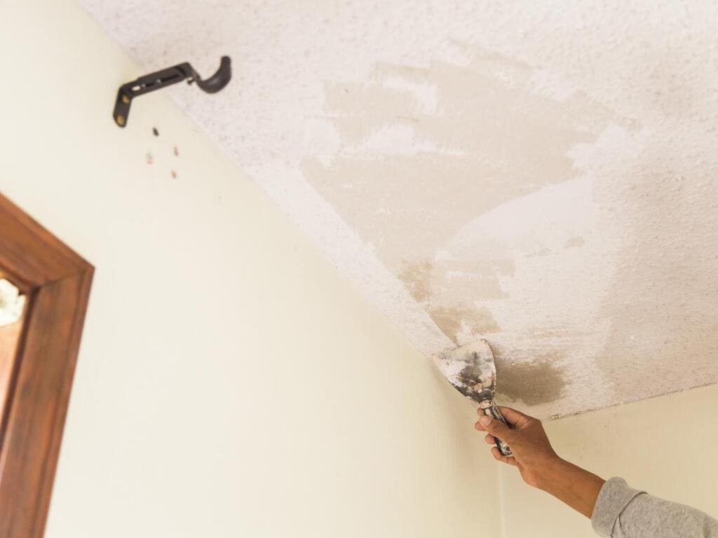 A person using a paint roller to paint a ceiling
