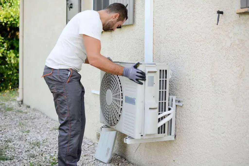 A man in white shirt and black gloves working on an air conditioner
