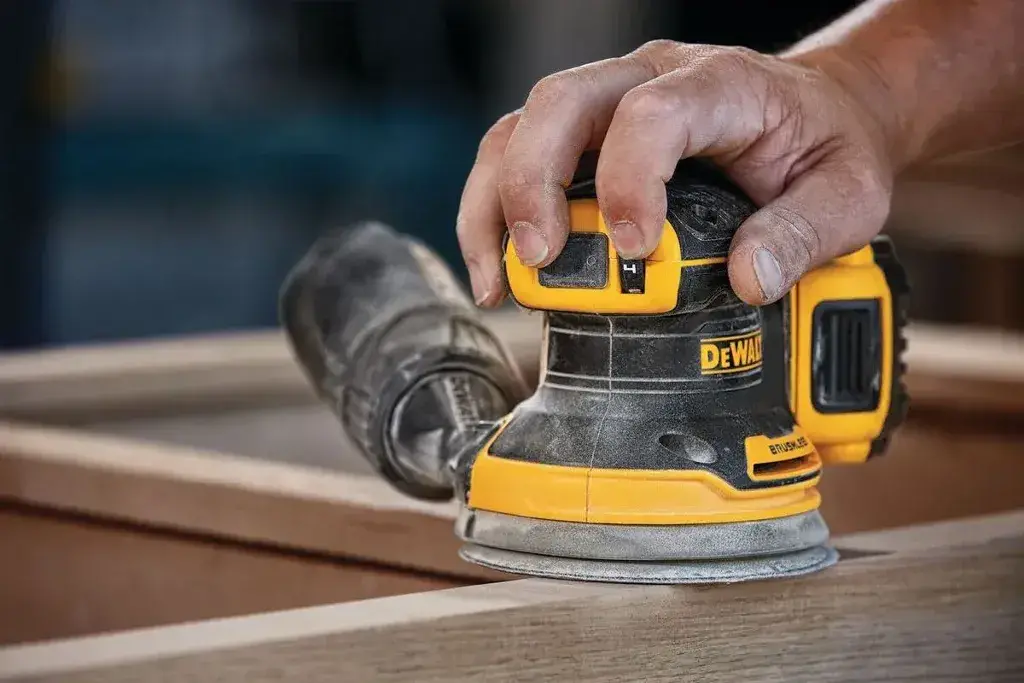 A person using a Orbital Sander on a piece of wood
