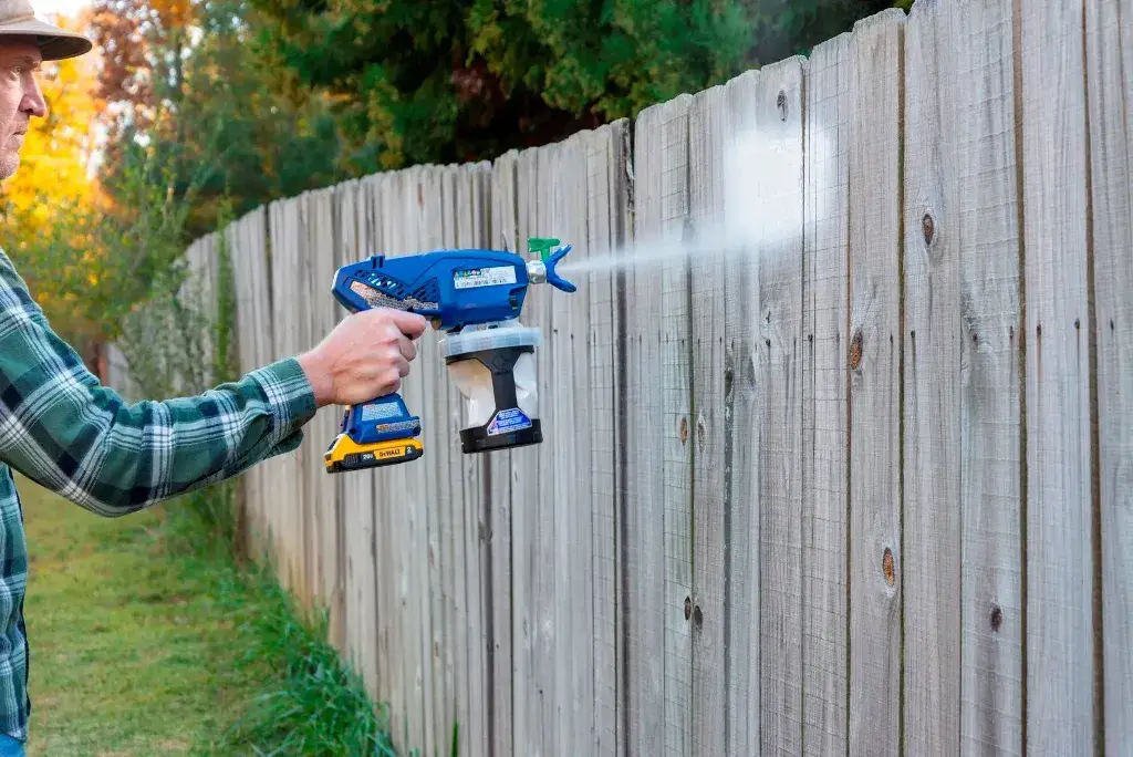 A man is using a Electric Spray Paint Gun on a fence
