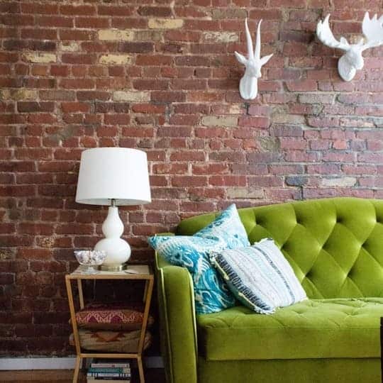 A green couch sitting in front of a brick wall
