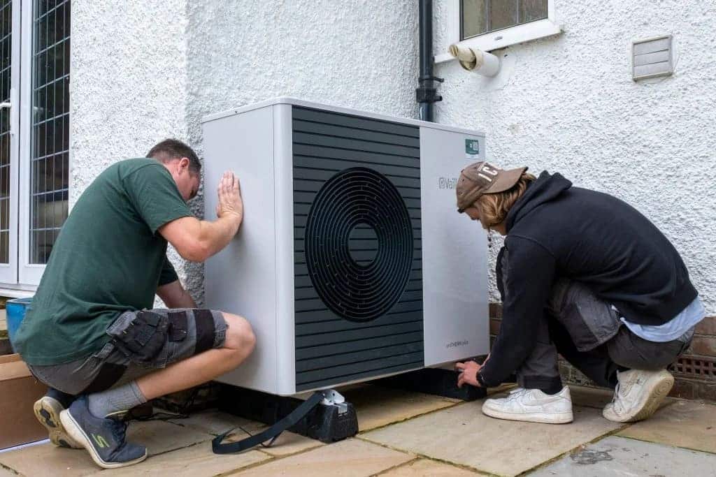 Two men working on an air conditioner outside a house
