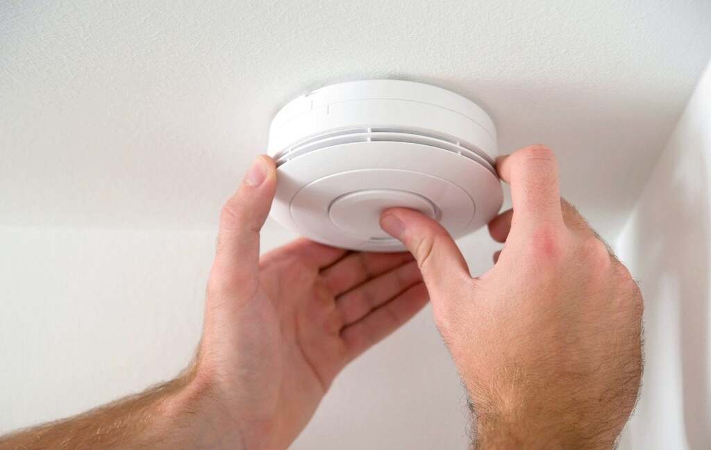 A man adjusting a smoke detector on a wall

